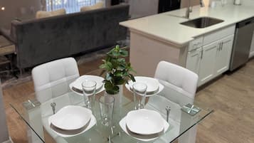 A modern dining area with a glass table set for four, white chairs, and a potted plant.