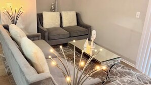 A modern living room with a grey sofa, a glass coffee table, and a decorative vase with lights. - 2 Bedroom 4 Min to Universal + Free Parking + Fast WiFi (Orlando)