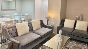 A modern living room with two grey sofas, a glass coffee table, and a dining area with a white table and chairs. - 2 Bedroom 4 Min to Universal + Free Parking + Fast WiFi (Orlando)