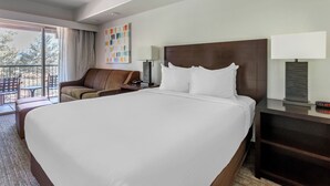 Ein Hotelzimmer mit einem großen Bett, einem Sofa, einem Schreibtisch mit Lampe und Blick ins Freie.