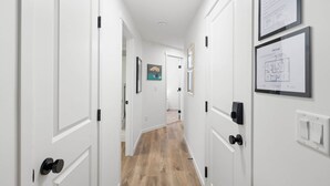 A hallway with white doors, a wooden floor, and framed artwork on the walls.