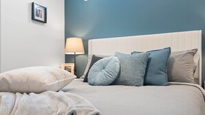 A neatly made bed with a white headboard and multiple pillows in shades of blue and grey.
