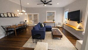 A modern living room with a sectional sofa, a dining table with chairs, a coffee table, and a TV mounted on the wall.