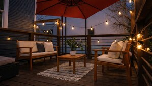 An outdoor patio with wooden furniture, a large red umbrella, and string lights.