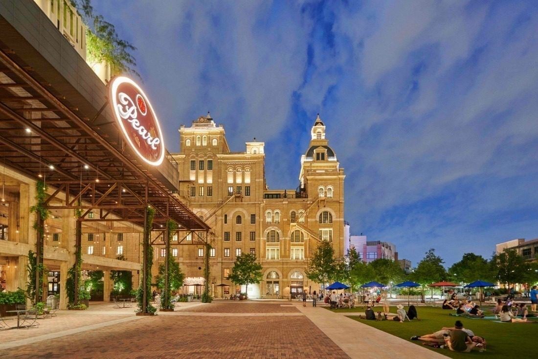 Un edificio grande e histórico con un llamativo letrero 'Pearl', rodeado de un amplio patio con zonas de estar y vegetación.