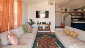 A living room with two sofas, a flat-screen TV, a coffee table, and a kitchen area in the background. - Flamingo Way | 2BR + Sleeping Den | Waterfront (Jamaica Beach)