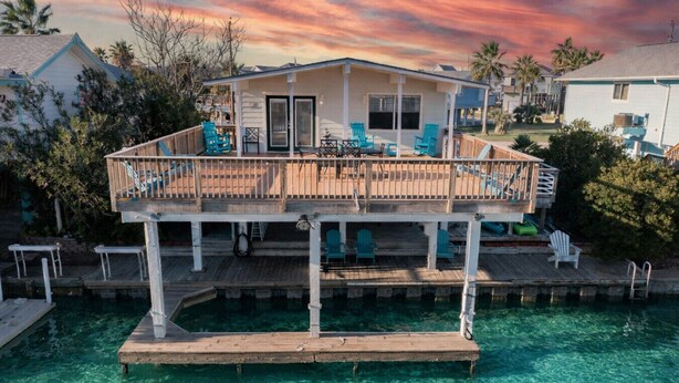 A waterfront property with a wooden deck, clear blue water, and a house with a balcony. - Flamingo Way | 2BR + Sleeping Den | Waterfront (Jamaica Beach)