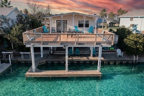 A waterfront property with a wooden deck, clear blue water, and a house with a balcony. - Flamingo Way | 2BR + Sleeping Den | Waterfront (Jamaica Beach)