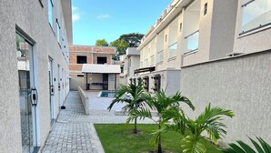 Um pátio com calçada pavimentada, palmeiras e piscina ao fundo.