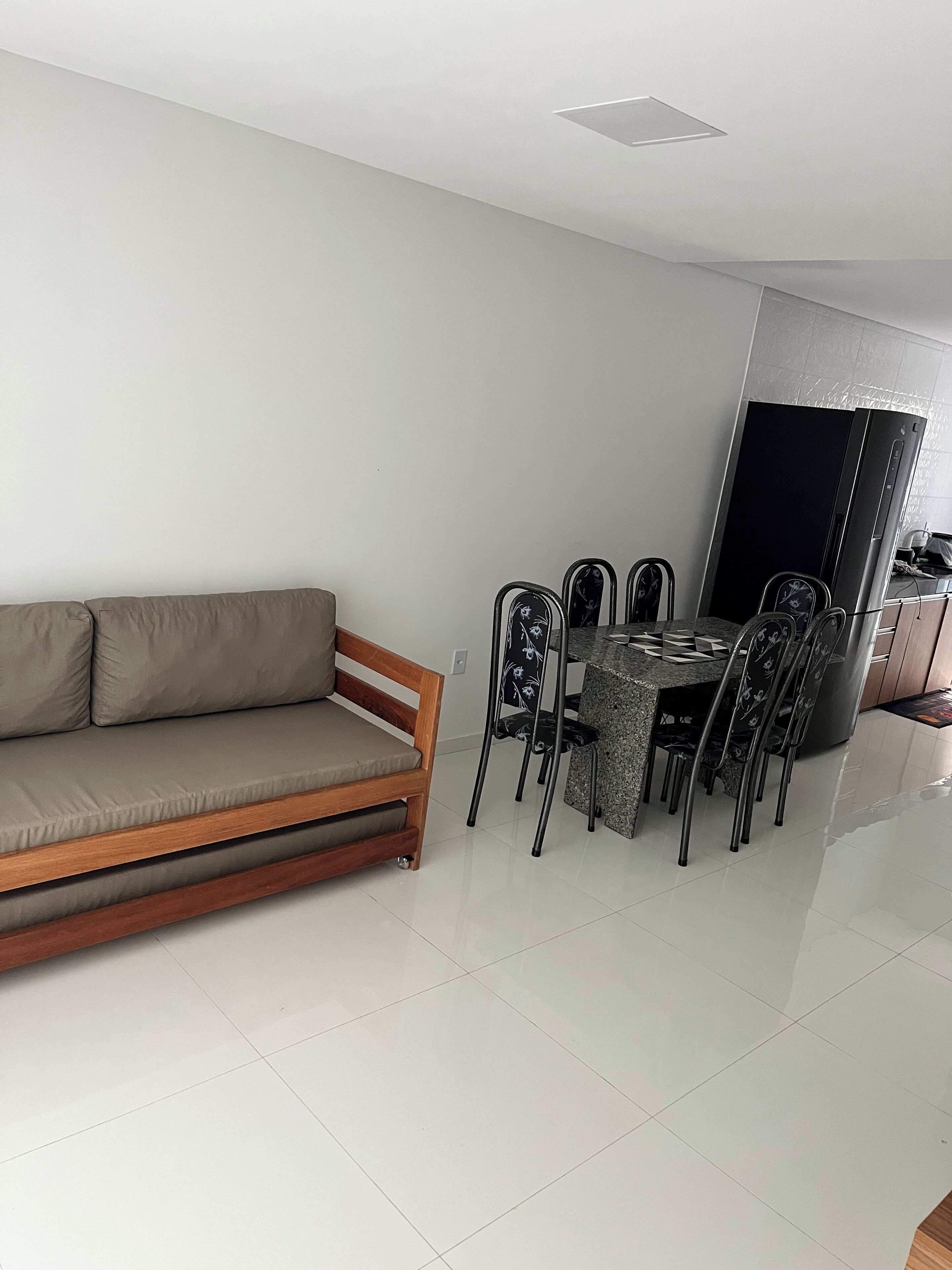 A modern living room with a sofa, dining table, chairs, and a refrigerator.