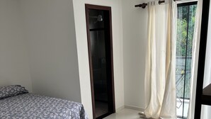 Quarto com cama, porta, janela com cortinas e varanda.