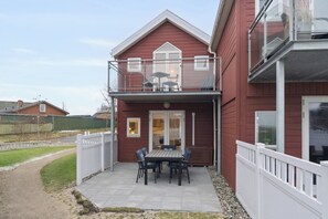 A red house with a balcony, a patio with a table and chairs, and a fenced yard. - Holiday apartment with sea view (Hadsund)