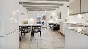 Una cucina moderna con mobili bianchi, una zona pranzo con tavolo e sedie, e un soggiorno con divano e tavolino.