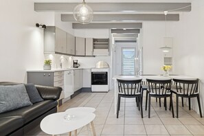 Una cocina moderna con armarios blancos, un sofá de cuero negro y una zona de comedor con cuatro sillas.