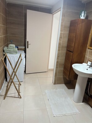 A bathroom with a white sink, a wooden cabinet, a towel rack, and a door. - Cosy T1 in the countryside (Sainte-Anne)