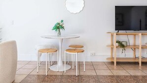 A modern living room with a round dining table, three wooden chairs, a white sofa, a TV on a wooden stand, and a mirror on the wall. - Boho Oceanview Getaway (Gold Coast)