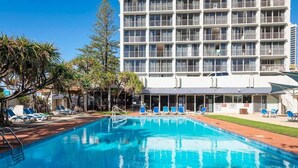 A hotel with a swimming pool, lounge chairs, and a tall building in the background. - Boho Oceanview Getaway (Gold Coast)