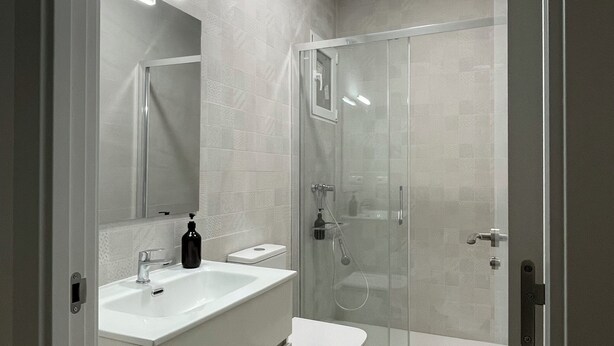 Ein modernes Badezimmer mit einer Duschkabine, einem weißen Waschbecken und einer Toilette.