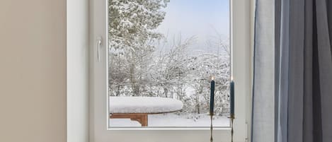 A window with a view of a snow-covered landscape, a candle holder, and a small shelf with a book and decorative items.