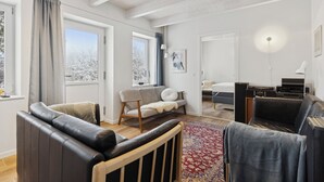 Una sala de estar moderna con un sofá, una butaca, un tapete y una cama al fondo.