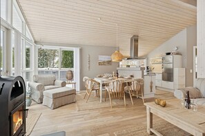 A spacious living area with a fireplace, dining table, and kitchen. - Holiday home with a covered terrace (Ålbæk)