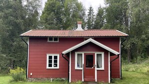 Ein rotes Holzhaus mit Satteldach, einer Haustür und einer kleinen Veranda.