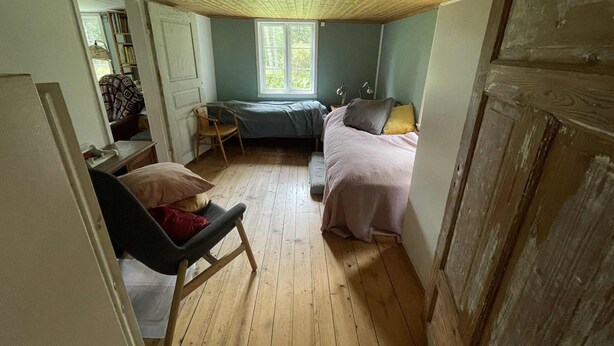 Ein Schlafzimmer mit Holzboden, einem Fenster, einem Bett, einem Sessel und einem Schreibtisch.