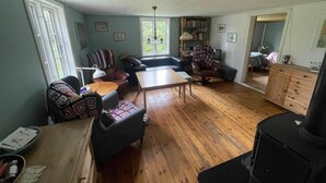 Ein gemütliches Wohnzimmer mit Holzboden, einer Couch, einem Sessel, einem Tisch und einem Bücherregal.