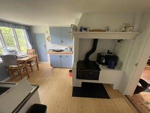 Una cuina compacta amb fogons, una zona de menjador amb taula i cadires, i una finestra amb cortines.