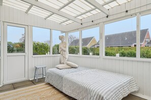Une chambre à coucher avec un lit, une statue, un tabouret et de grandes fenêtres.