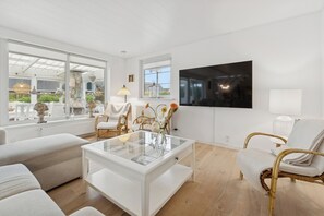 Un salon moderne avec une table basse en verre, des fauteuils en osier et un grand téléviseur fixé au mur.
