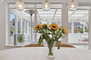 Un coin repas comprenant une table, des chaises, un vase avec des tournesols et une vue dégagée grâce à de grandes fenêtres.