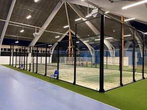 Ein Sporthaus mit Tennisplatz, Sitzbereichen und hohen Decken mit Beleuchtung.