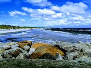 A beach with rocks in the foreground, a sandy shore, and the ocean in the background. - Cozy holiday home with spa and fireplace (Ålbæk)