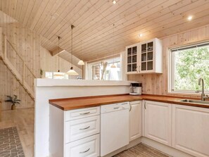 A kitchen with white cabinets, a wooden countertop, a built-in dishwasher, and a window with a view of greenery. - Cozy holiday home with spa and fireplace (Ålbæk)