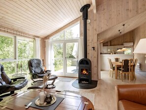 A cozy cabin interior with a fireplace, wooden furniture, and large windows. - Cozy holiday home with spa and fireplace (Ålbæk)