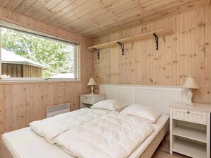 A wooden-paneled bedroom with a bed, bedside tables, and a window. - Cozy holiday home with spa and fireplace (Ålbæk)