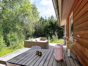 A wooden deck with a table, two chairs, a wicker sofa, and a pink lantern. - Cozy holiday home with spa and fireplace (Ålbæk)