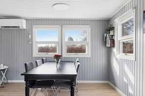 A dining room with a large table, two windows, and an air conditioning unit. - Cosy holiday-house with annex close to the see (Hals)