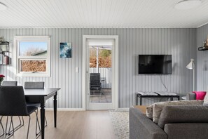 A modern living room with a dining area, a TV mounted on the wall, and a view through a glass door. - Cosy holiday-house with annex close to the see (Hals)