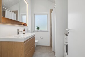 Une salle de bain moderne avec un meuble-lavabo en bois, un grand miroir, des toilettes et un lave-linge.