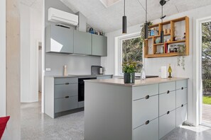 Una cocina moderna con armarios grises, una isla central y un estante de madera con diversos objetos.