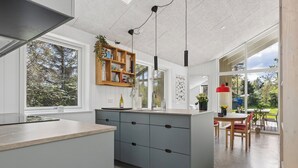 A modern kitchen with a central island, built-in shelves, and a dining area with a table and chairs. - Cozy little cottage, close to the Limfjord (Storvorde)