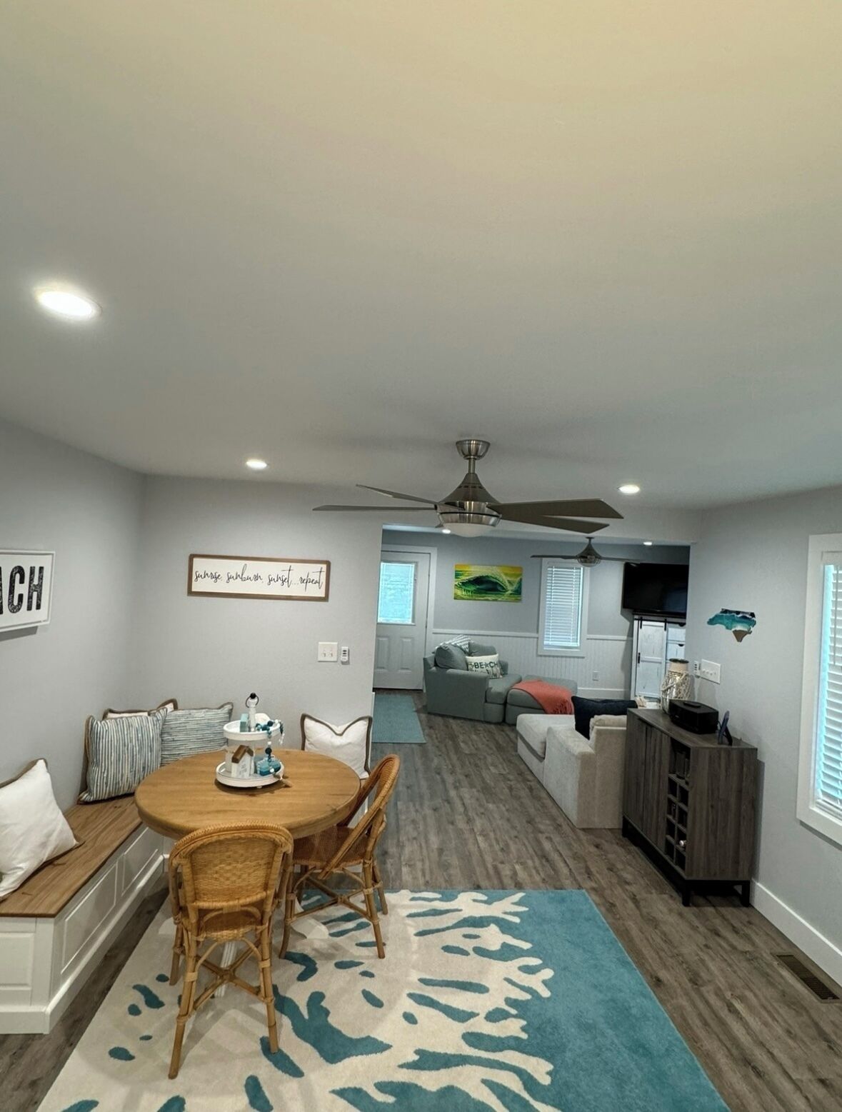 A modern living room with a dining area, a ceiling fan, and a television.
