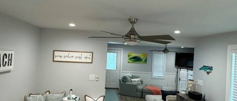 A modern living room with a dining area, a ceiling fan, and a television.