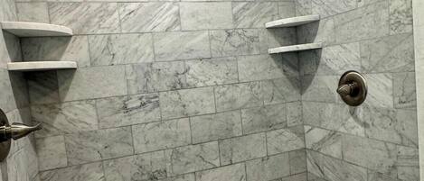 A shower with marble tiles, a handheld showerhead, and a pebble-patterned floor.