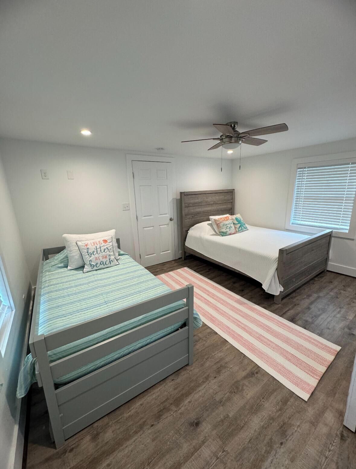 A bedroom with two beds, a ceiling fan, and a window with blinds.