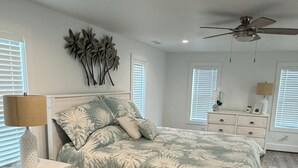 Een slaapkamer met een bed, nachtkastje, dressoir, plafondventilator en wanddecoratie.