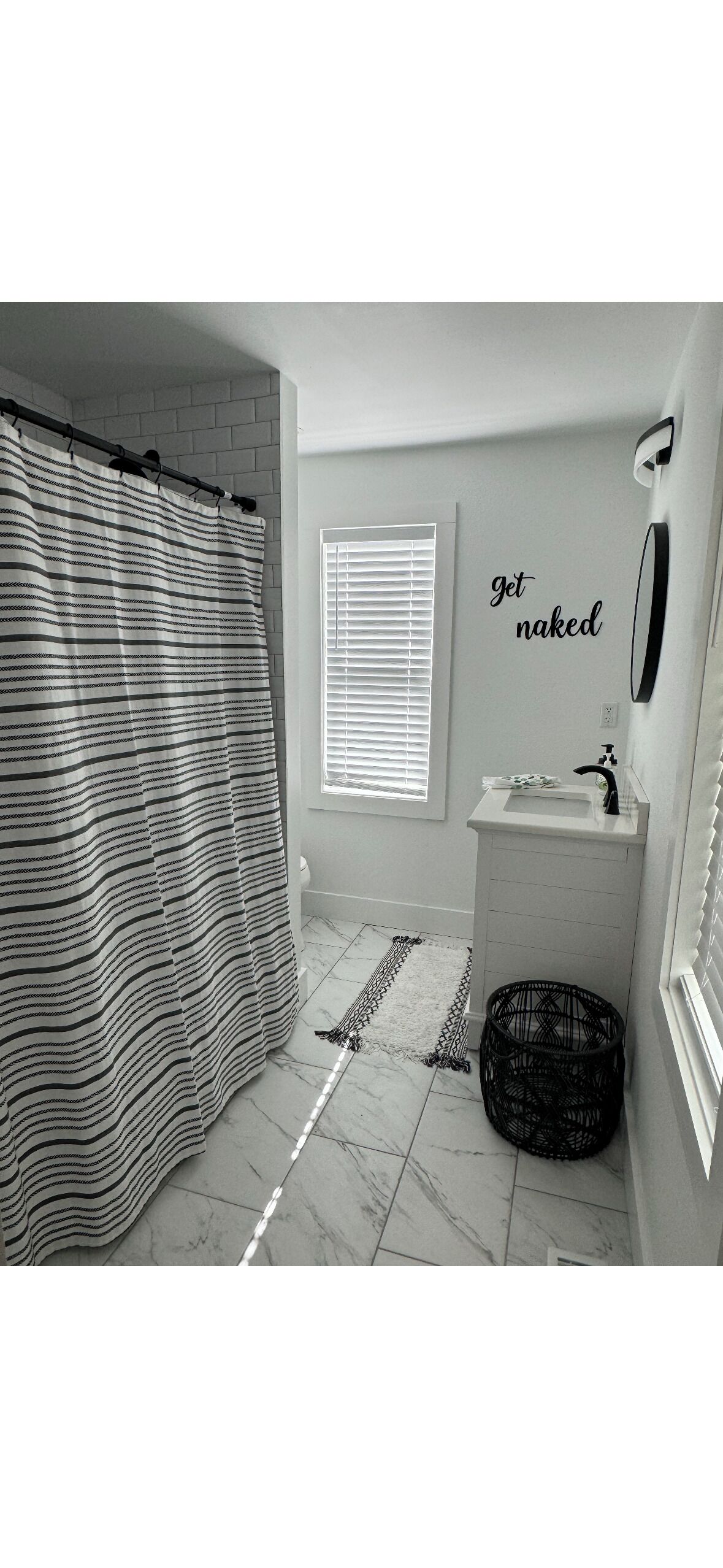 A bathroom with a striped shower curtain, a sink, a mirror, and a window with blinds.