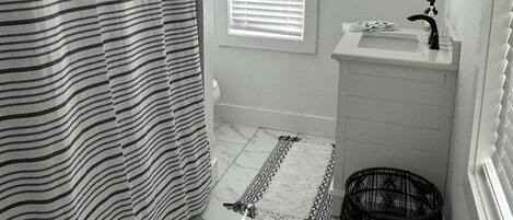 A bathroom with a striped shower curtain, a sink, a mirror, and a window with blinds.